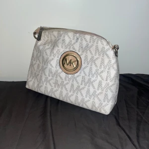 Snygg MK väska - En snygg michael kors väska som inte längre kommer till andvändning här hos oss. Bra skick men tidigare andväns som smink väska så är lite smutsig på insidan men ska vara lätt att bara tvätta bort i tvätt maskin eller med smink borttagning. 