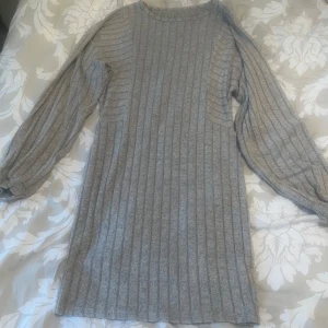 Grå stickad klänning - En bekväm grå stickad klänning med långa ärmar. Klänningen har ett ribbat mönster och är perfekt för kyligare väder.