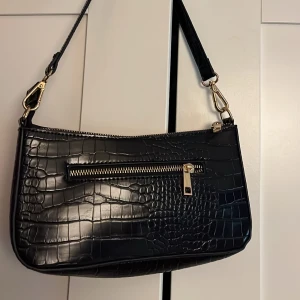 Axelväska/ Handväska  - Axelväska/Handväska med kort axelband i konstläder med ett litet ytterfack fram, också använd fåtal gånger 