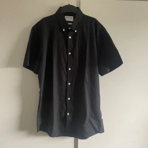 Svart kortärmad skjorta från Lindbergh - En svart kortärmad skjorta från Lindbergh med vit knappstängning. Skjortan är i slim fit och tillverkad av en blandning av bomull och linne. storlek m. bra skick 
