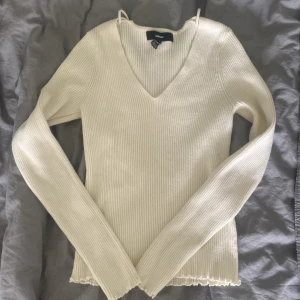 Vit ribbad tröja från Vero Moda - En vit ribbad tröja från Vero Moda med v-ringning. Tröjan har långa ärmar och en vågig kant vid ärmslut och nederkant.