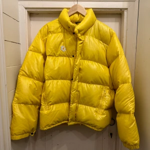 MONCLER VINTAGE - MONCLER dunjacka i härlig gul färg. Strl 3. (Upplevs som en rymlig 38/40) Förra ägaren har sprättat bort Monclermärket på armen (se bild) samt gjort en lagning på framsidan där nu en broderad blomma sitter. Jackan är i fint skick.