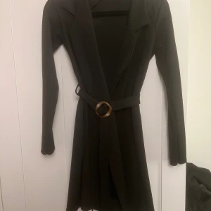 Svart klänning med bälte  - Svart klänning i mjukt material med tillhörande bälte i midjan. Slutar lite ovanför knät på en som är 160 cm lång. Använd 1 gång.