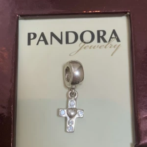 Pandora berlock nyskick retired  - Berlock i sterling silver,aldrig använt. Legat i original förpackning tillsammans med andra berlocker sen 2005/06. Ingen egen ask. Tillverkas ej mer. Märkt 925/ALE (pandoras stämpel) Heter: Retired Sterling Silver Cross Dangle with Clear Zirconia - 790355