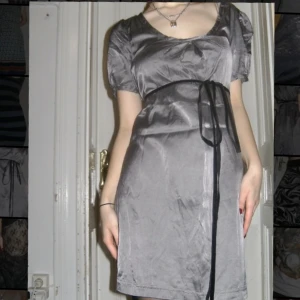 Satin miniklänning - Grå satin miniklänning med fastsydda sammetssnören. Jättesöt med många sätt att styla. Färgen är grå-lila. Stl M men passar mig som är S.  Skriv för mått. Priset kan diskuteras. Köparen står för frakten men kan även mötas upp på Södermalm i Stockholm. 