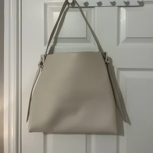 Väska - Rymlig väska från Mango! Beige färg med ett fack med dragkedja i mitten som en neccesär. Får plats med mycket i! 