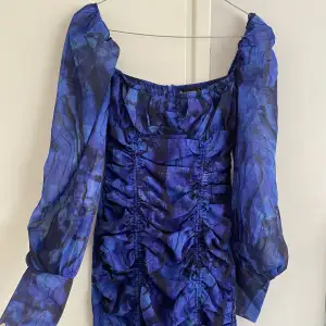 Mörkblå mönstrad klänning med knytdetaljer och puffärmar, dragkedja baktill. 