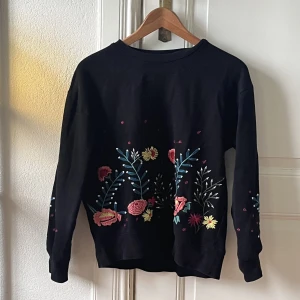 Sweatshirt  - Svart sweatshirt med broderade blommor på. 