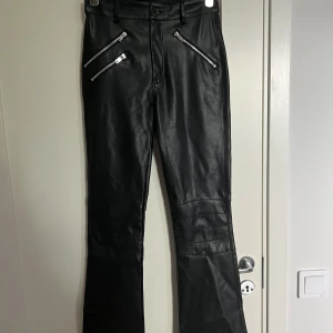Byxor  - Flared byxor i läderimitation från bikbok. De sitter mycket fint förutom att en del av bälteshällorna är sönder. De har även en fläck på framsidan (bild 3) men det syns mycket mindre i verkligheten än på bild. Midjemått: ca 34cm, Innerbenslängd: ca 77cm 