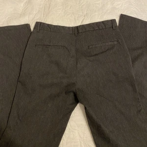 Lågmidjade kostymbyxor - Gråa kostymbyxor i randigt tyg.  Midja 76 cm, ben 81 cm. 