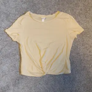 En superfin gul T-shirt i en ljusgul färg och med en knytning framtill. Är i storlek XS från H&m. 