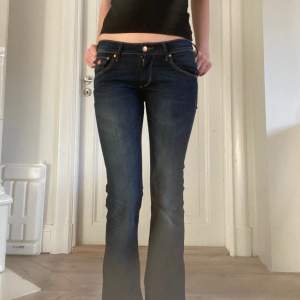 Mörkblåa lågmidjade bootcut jeans med snygga detaljer och bakfickor. Midjemåttet är 36.5 och innerbenslängden är 77cm