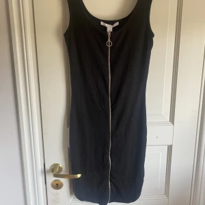 Svart klänning - Svart klänning från Nelly med dragkedja framtill i stretchigt material. Klänningen är i storlek S och oanvänd, prislapp kvar.