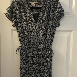 Klänning - Svart och vit blommig klänning som går till knäna och knyte på sidorna som man kan se på andra bilden