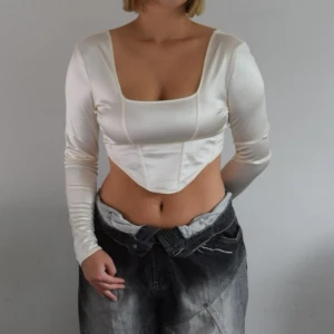 Champagnefärgad satintopp - Strl: M Mått: ärmlängd 45cm, längd fram 46cm, längd bak 36cm Material: 95% polyester, 5% elastan Modell: åtsittande kort topp, långärmad med fyrkantig urringning  Märke: H&M Skick: använt skick, finns tecken på användning i form av någon lös tråd 