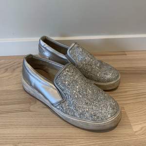 Glittriga silver slip-on skor i storlek 38. Bra skick. Använt de några enstaka gånger. Innersula i läder. 