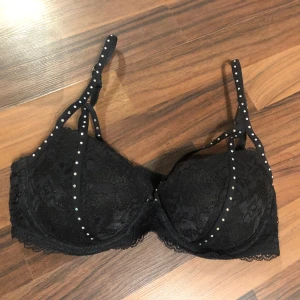 Svart spetsbh med rhinestones  -  Svart bh med rhinestones. Ena remen lägger sig snyggt över bröstet. Strl 75B/80B. Bra skick.  Frakt på 69kr tillkommer.