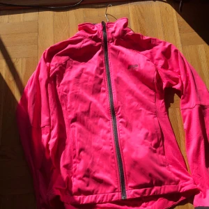 Rosa träningsjacka - Denna rosa träningsjacka är bara använd vid ett tillfälle och har tyvärr en liten svart fläck på axeln (som ni kan se på bilden ovan). Annars är den i fint skick och har flertal reflexer inklusive längs dragkedjan.