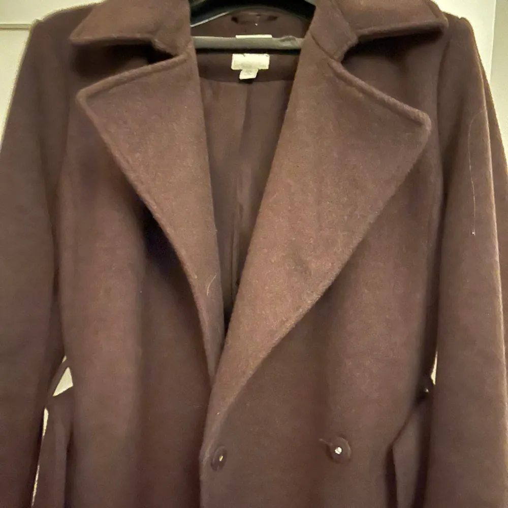 En brun kappa från HM med ett skärp i midjan, väldigt gott skick då den endast är använd ett fåtal gånger.. Jackor.