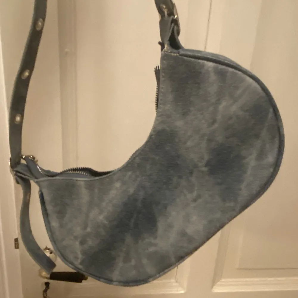 En blå axebandväska med metal detaljer på. Minns ej var den är ifrån. Den kommer inte till användning eftersom jag ej använder den.. Väskor.