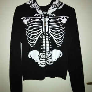 Skeleton / skelett hoodie / zipjacka från Living Dead Souls, Svart,  Strlk: Small. Fint skick. - Skeleton / skelett hoodie / zipjacka från Living Dead Souls, Svart, Strlk: Small. Fint skick. Har luva med dragkedja hela vägen upp, med snygg liten silvrig döskalle som hänger på själva dragkedjan. Inga fickor men tumhål finns. Felfritt skick.