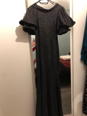 Balklänning - Säljer maxi klänning i väldigt bra skick, använd enbart en gång. Svart färg, med glitter. Liten v-öppning i ryggen annars täcker den bra över bysten. 