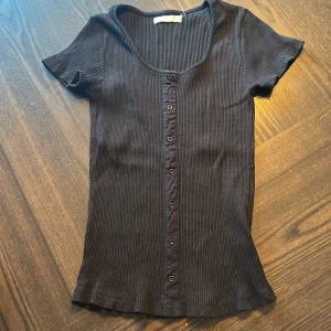 Svart t-Shirt med knappar - De är en svart t-Shirt med knappar, otroligt stretchig. Passar storlek XS/S men säkert också XXS. Märket på tröjan är jag osäker kring.