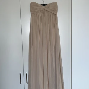 Balklänning/långklänning - Rosa beige balklänning från NLY TREND. Använd ett fåtal gånger och har en liten fläck som tyvärr inte går bort i tvätten men syns inte vid användning. Jag är 170 cm och kunde ha den med klackar. 