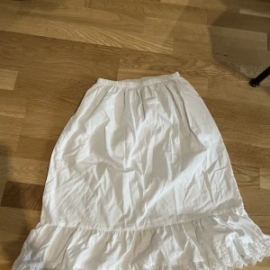 Vit kjol med spets - Vit knälång kjol med spets och resårband vid midjan. Använd ett fåtal gånger men inga defekter 