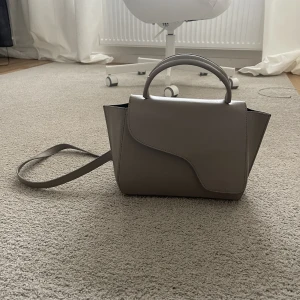 ATP atelier väska - Säljer min fina ATP väska i beige/grå färg då jag inte får någon användning av den. Väskan har några mindre defekter som syns på bilderna. Defekten på bandet syns inte när man bär väskan eftersom det är på sidan mot kroppen. Annars väl omhändertagen.