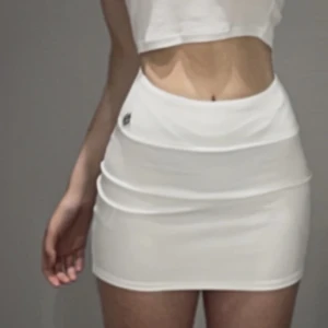 Vit tennis minikjol med en silver brosch 💕 - En kortkjol/minikjol i vitt, men silver broschyr på höften.  Y2k stil/ 2000s/ 90s Trendig och jätte fin! Har aldrig använt, bara testat (på bilderna) Jätte skönt material i silke. Helt ny, utan prislapp Lågmidjade och tajta u formen :))❤️ Storlek XS/S