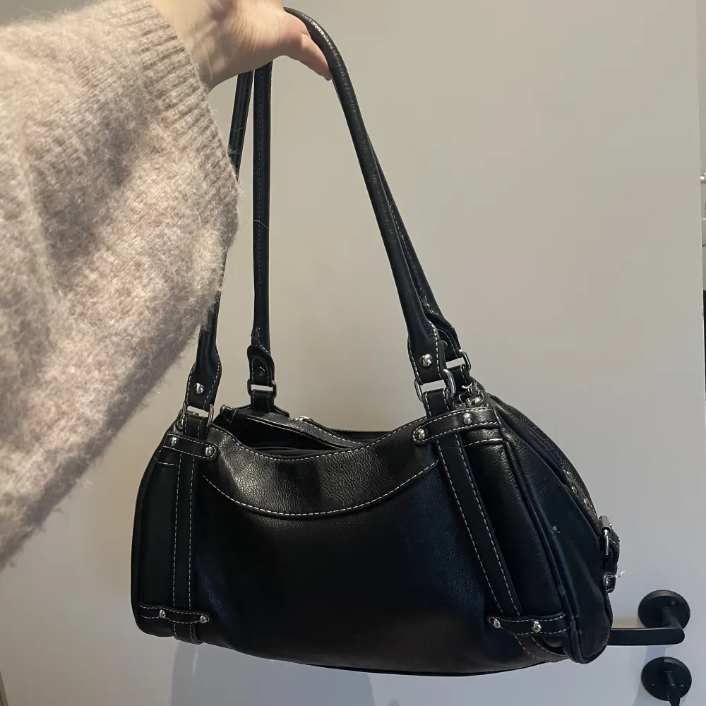 En svart liten/medel handväska i svart ”läder/skinn”. Silvriga detaljer och väldigt rymlig med många fickor inuti. Knappt använd, fint skick. Osäker på märke då den är köpt här på plick.. Accessoarer.