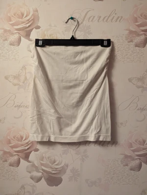 Vit tubtop - En vit tubtop/ärmlöst linne i ett tjockare mjukt stretchigt tyg. Sparsamt använd. Dubbelt tyg vid bysten för extra stöd.