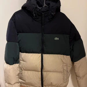 Lacoste Dunjacka - En väldigt fin dunjacka av märket Lacoste. Inga skador eller fläckar. Mycket bra skick 8/10. Använd en säsong men säljer då jag köpt en ny vinterjacka och den inte används. Slutsåld modell men pris var runt 4000!