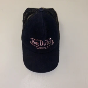 Von Dutch Keps - Säljer denna söta Von Dutch Cap! Svart velor material smyckad med ljusrosa text. Har ett flaw där man justerar storleken, men inget som får kepsen att trilla av eller sitta dåligt när den är inställd så som på bilden (minsta storlek). 