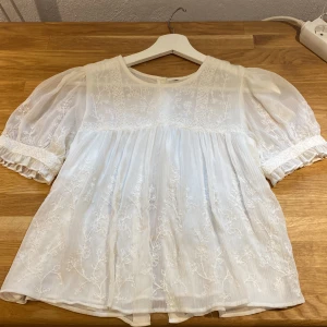 Vit blus med mönster  - En jättefin vit blus med mönster på framsidan och en knäppning på baksidan, säljer den då den blivit för liten.. 