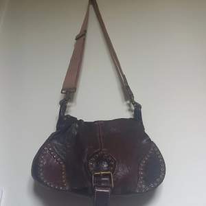 Boho style purse with bronze metal studs. Adjustable length for strap. 2 pockets. Main pocket has a zipper pocket. 