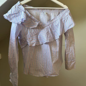 One shoulder blus - Jätte fin blå one shoulder blus med vita och röda ränder, Från Nelly. Använd ett fåtal gånger. Är för lång för mig i ärmarna då jag är 145. (Förlåt för att den är så skrynklig🩷)