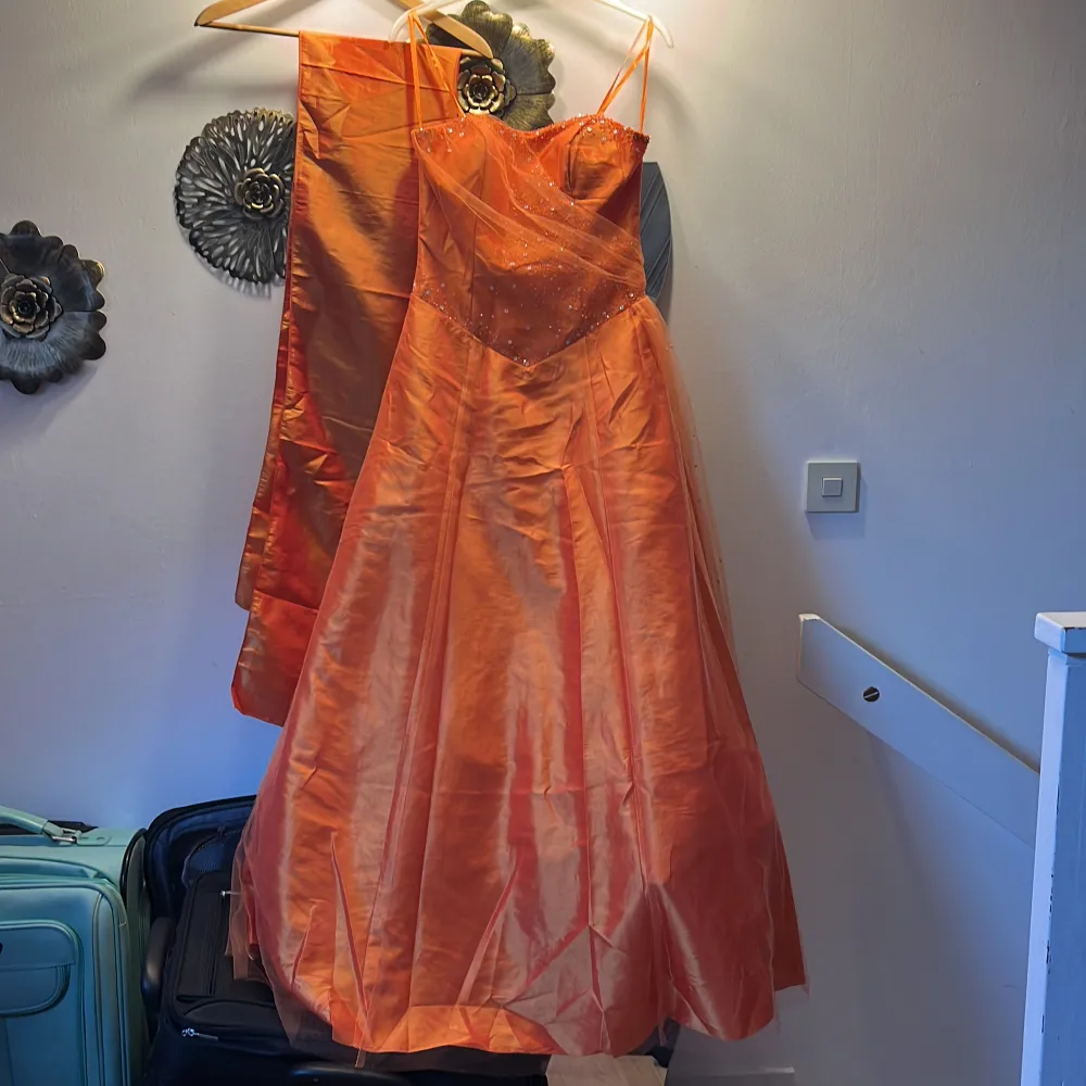 Orange balklänning som har en korsettliknande överdel. Har även en extra sjal som är cirka 2 m i längd och 50 cm i bredd. Finns extra tyg undertill som gör den  puffig men det är enkelt att ta bort ifall man önskar. Skriv vid behov av fler bilder☺️. Klänningar.