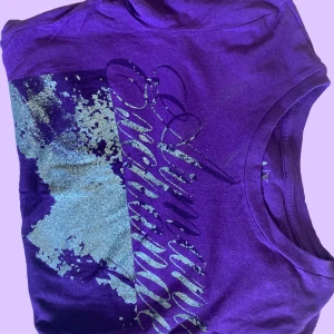 Armani exange T shirt - En mörk lila armani T shirt som sitter ganska fint på kroppen, lite glitter har fallit av men Fortfarrande jätte gullig, nästan aldfig använd eftersom jag köpte den second hand.