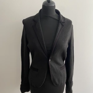 Tätstickad kavaj  - Tätt stickad kavaj från MQ STOCKH LM i Strl S. Färg är mörkgrå med svarta kanter. Lapp avtagen men aldrig anvöndz 