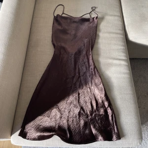 Brun silkeklänning  - En brun silkes klänning med öppen rygg! Formar midjan/kroppen. Storlek 34/S. Tejpen går att ta bort ( tar lite tid), därmed billigare pris. Längd 75cm