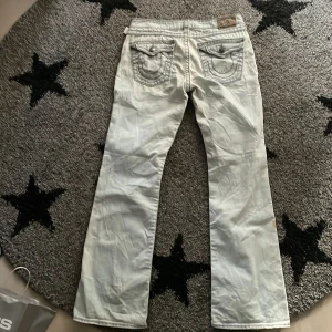 True Religion jeans - Vit/gråa True Religion Jeans med mörkgrå stitching. 32 i midjan och passar i längden på mig som är 192 cm lång  Säljer för att råkade köpa dam modell