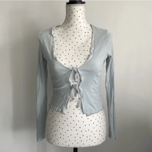 Babyblå blus/topp - Ginatricot  - En jättegullig topp från Ginatricot, endast använd EN gång, som helt ny. Original pris 249kr men säljer för 99kr då den inte kommer till användning🥲. Skulle nog säga att det passar alla mellan XS-M för man kan justera själv. Storlek S.