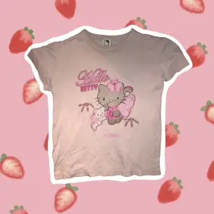 Figurnära Hello Kitty T-shirt, ljus rosa. Det syns knappt på bilderna med nedersta sömmen och allt motiv på T-shirten glittrar lätt. Jag på bild har storlek M. Armarna på T-shirten är bortklippta och har inte ömsat.  