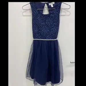 En marinblå klänning med spets på överdelen och glittriga prickar på. Sedan en kjol med tre lager olika tyger. Perfekt för ditt barn att ha på sin födelsedag eller någon annan fest. 