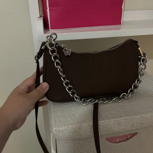 Jättefin väska❤️ - Jättefin väska från Bershka, aldrig kommit till användning❤️ den har en jättegullig fjäril på dragkedjan, det går att ta av den vanliga bandet och kedjan om man vill, man ser de på bild nummer 3❤️ den är brun men ser väldigt mörk ut på bilden