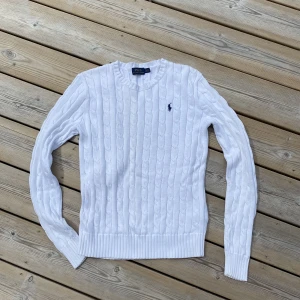 Polo Ralph Lauren, kabelstickad tröja - Kabelstickad tröja från Polo Ralph Lauren. Vit, med marinblå logga på bröstet. 100% bomull. Strl S, men ganska liten i storlek, mer som XS. I mycket gott skick. 