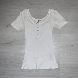 Vit topp med knappt - Vitt topp med knappad från Pieces. Ribbat stretchigt material. Den är i bra skick. Nypris 149kr. Storlek S.