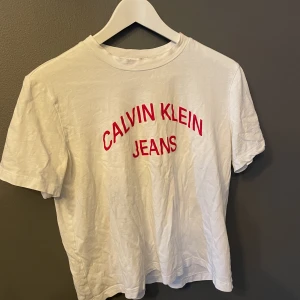 Calvin Klein t-shirt  - Vit t-shirt med röd text. Nästintill oanvänd. Kortare modell  Skulle uppleva den mer till en S än M 
